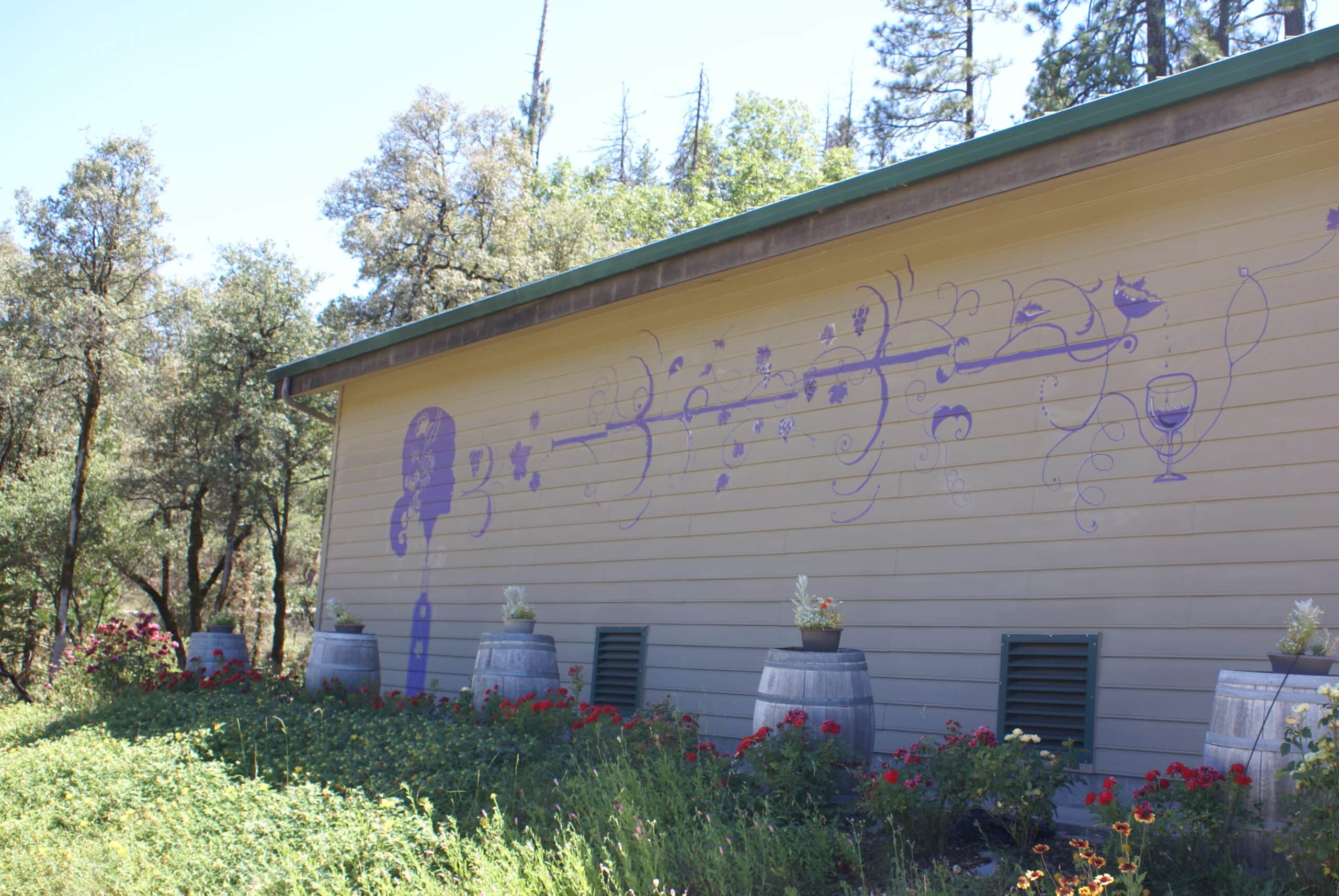 Exterior view of Vanguardia Wines building with musical notes mural and wine barrels in a garden setting.